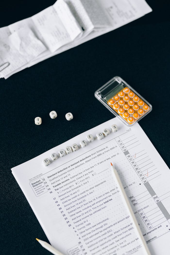 Gallery-1 Flat Lay Of Tax Documents, Calculator, And Labeled Deductions On A Black Background.