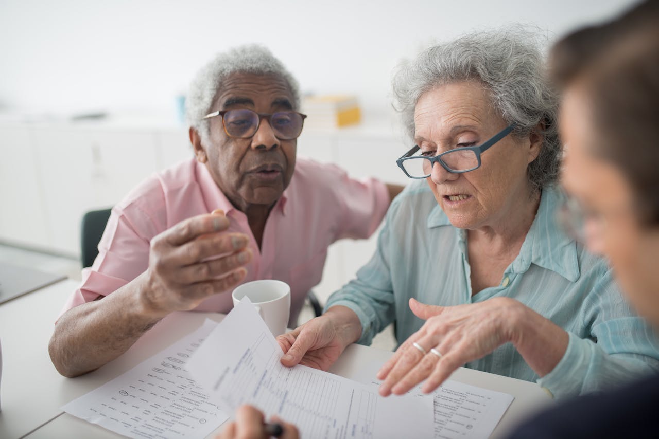 About-01 Elderly Couple Discussing Financial Documents With A Consultant In An Office Setting.
